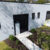 Light gray industrial building with black doors and small barred windows, number 615, a concrete walkway, and mulched landscaping.
