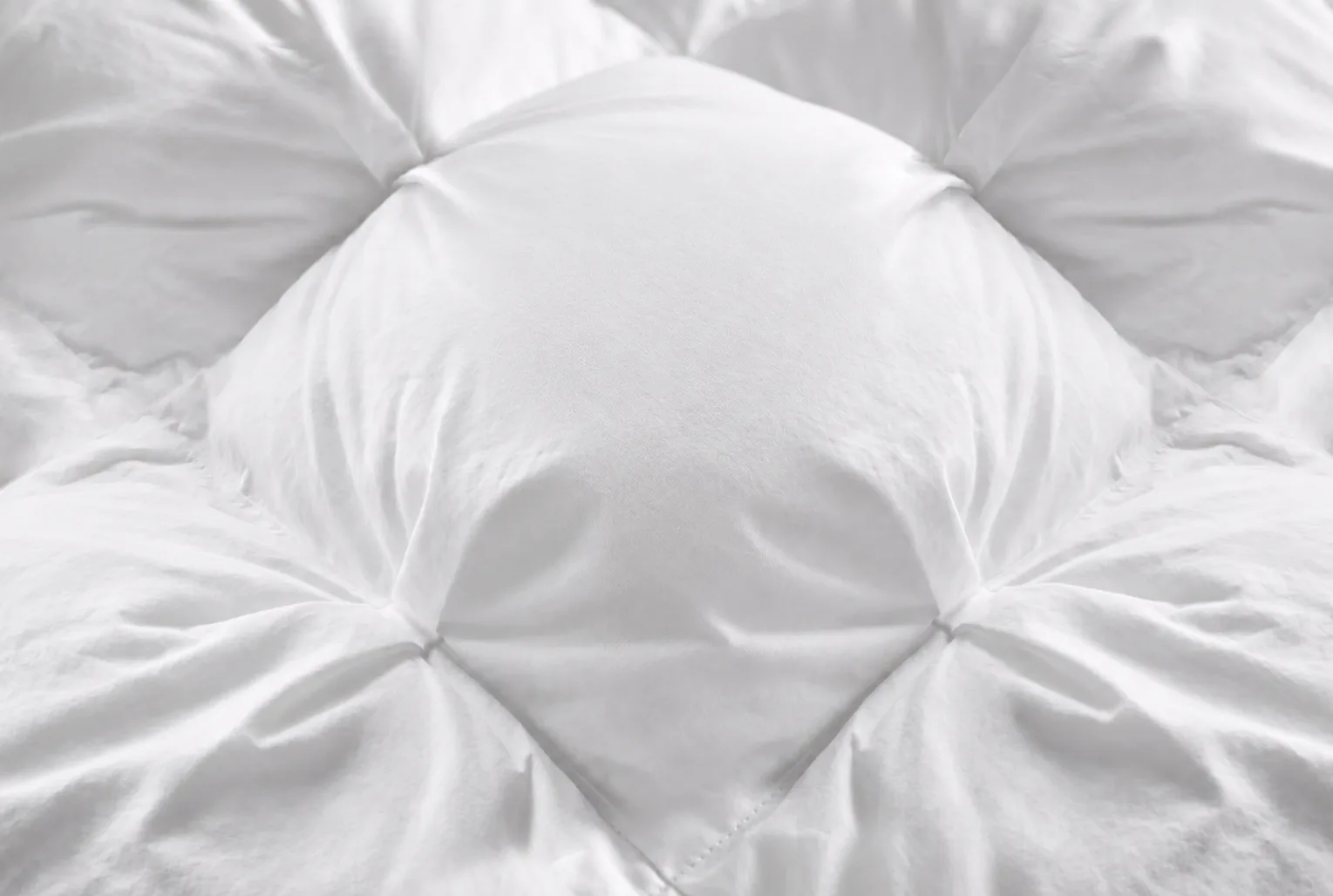 Close-up of a white quilted duvet with a diamond-tufted pattern.
